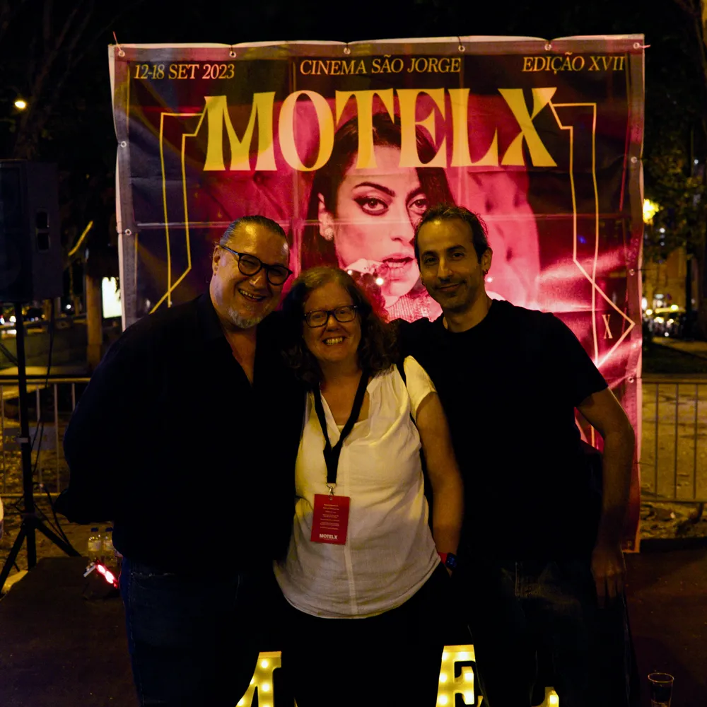two men and a woman posing in front of a poster
